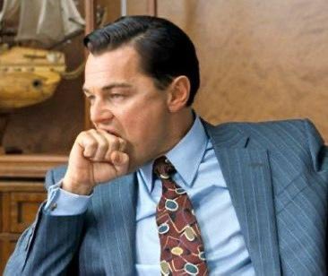 A man in a blue pinstripe suit and patterned tie sitting thoughtfully with his hand near his mouth, resembling a famous movie still.