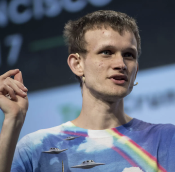 Vitalik Buterin, Ethereum's co-founder, is pictured at a tech conference wearing a U.F.O.-themed tie-dye t-shirt, gesturing as he speaks. The image accompanies a post about his proposal for EIP-8288, which could enhance Ethereum's cryptographic flexibility.