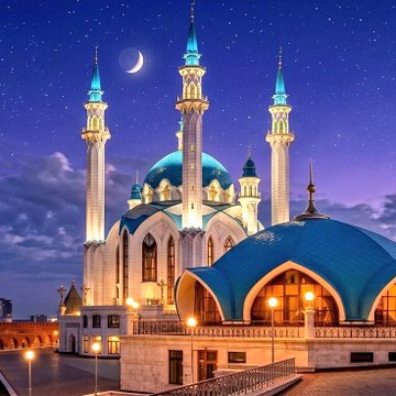 The image features a large mosque with blue domes, surrounded by white buildings that have blue roofs. The mosque has four distinct towers, each topped with a dome, creating an impressive architectural structure. The sky above the mosque is dark, suggesting either nighttime or a cloudy day. In the foreground of the photo, there are street lights and lampposts illuminating the area around the mosque. The image also contains text that reads "LATEST- Builders live meetup with @Casper_Network at @IstanbulBlockWk and $CSPR is ready for vertical breakout".