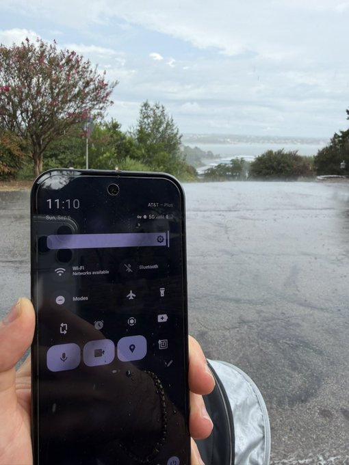A hand holds a phone displaying a quick settings menu with the time "11:10," "Sun, Sep," and "AT&T - Plus" carrier visible, set against a scenic overlook view of a distant landscape with trees and water. The image illustrates a real-world test of a Voidmob eSIM service activated on a GrapheneOS device, with the phone's active mobile connection demonstrating the service's functionality in an outdoor location.
