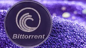 A close-up of a coin displaying the "BitTorrent" logo with a stylized wave design, set against a glittery purple background, visually representing the platform's milestone of 581,384,265 client installations highlighted in the post about its network effect.