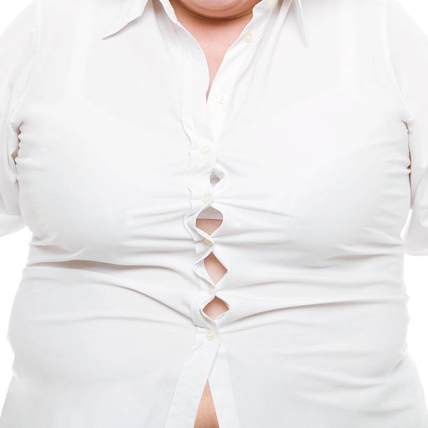A close-up of a person wearing a white button-up shirt that is straining at the buttons due to their larger size, with multiple buttons pulling apart and creating gaps in the fabric.