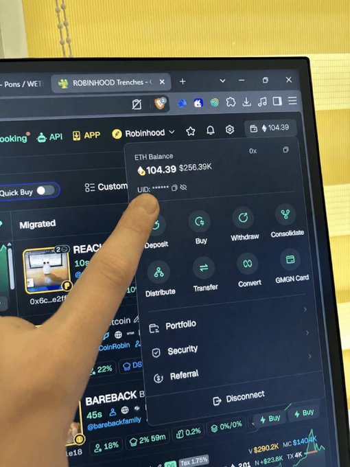 A finger points at a laptop screen showing a crypto wallet dashboard with an 'ETH Balance' of 104.39 ($256.39K) and a dropdown menu featuring Deposit, Buy, Withdraw, Consolidate, Distribute, Transfer, Convert, and GMGN Card options.