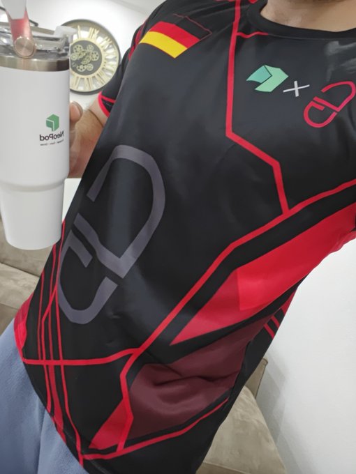 A person holds a white tumbler branded 'boffos' next to a black and red jersey featuring a German flag patch and a crossed-out German flag logo.