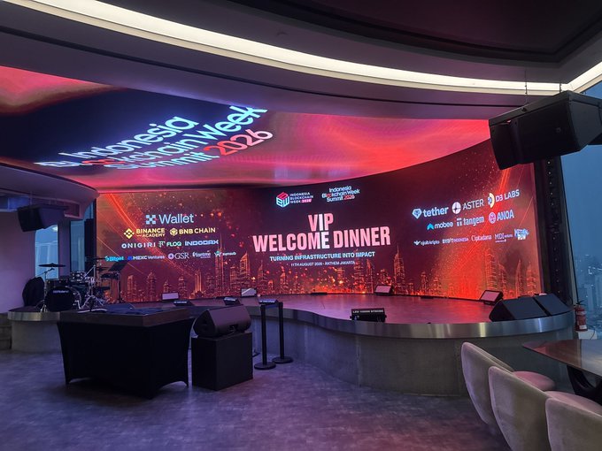 A photograph of an event space set up for the "Indonesia Blockchain Week 2025," featuring a large LED screen displaying "VIP WELCOME DINNER" alongside various crypto sponsor logos including Binance, BNB Chain, Tether, and OKX.