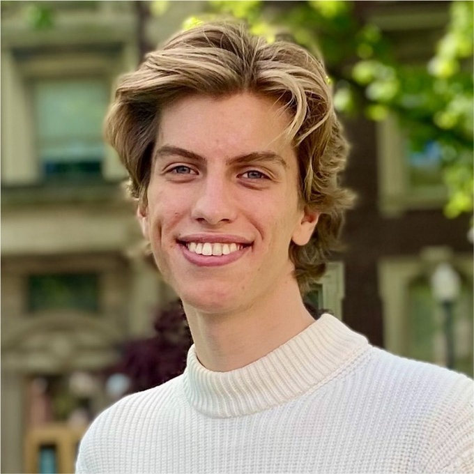 A smiling young man with blond wavy hair wearing a cream-colored knit sweater poses for a portrait outdoors, with the motivational caption suggesting his confident appearance embodies the financial success promised to followers. The image appears to be a typical lifestyle or finance influencer photo used to attract engagement on social media.
