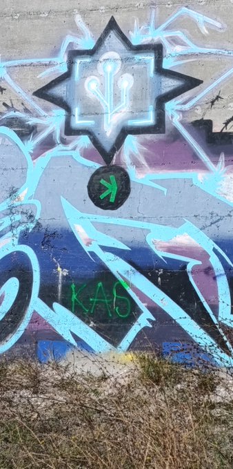 A piece of graffiti on a wall featuring a star-like emblem with glowing lights, abstract blue designs, and the green text "KAO" at the bottom.