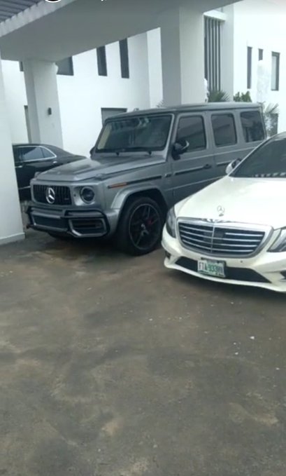 A grey Mercedes-Benz G-Wagon and a white Mercedes-Benz S-Class parked in a driveway of a white house.