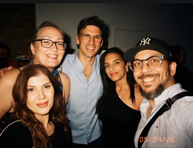 A group selfie of five people smiling together at what appears to be a social event, with a date stamp reading '09/04/26' in the corner.