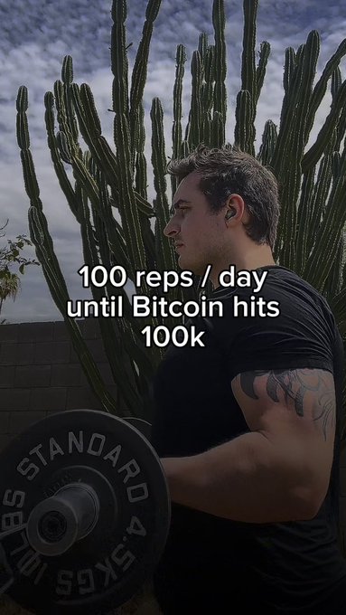 A man lifts weights outdoors near cacti, with text overlay reading '100 reps / day until Bitcoin hits 100K'.