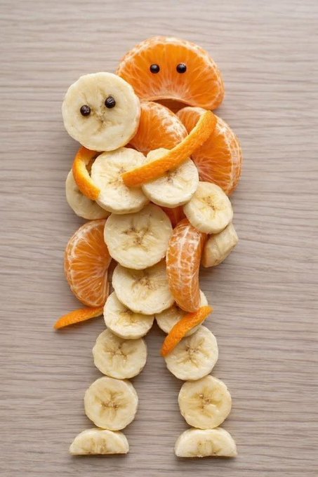 An arrangement of banana slices and mandarin orange pieces on a wooden surface, creatively assembled to look like a person.