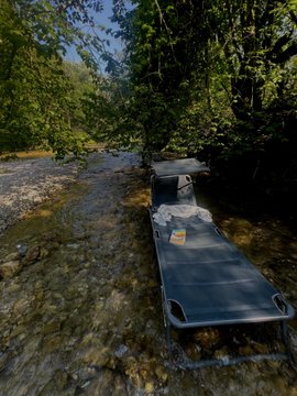 A cot and camping setup is staged along a shallow, rocky creek surrounded by dense green forest in Bavaria, with a Starlink satellite internet dish visible on the gear—capturing the off-grid, remote-work vibe behind the "Bavarian nature + Starlink = perf Solana Summer" caption.