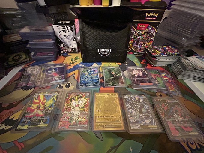 A collection of Pokémon trading cards, including several holographic and gold cards, displayed on a colorful surface with stacked card storage boxes in the background.