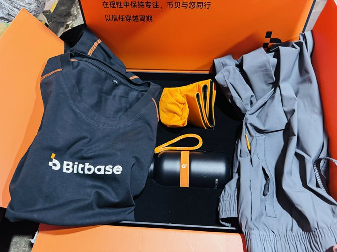 An open orange gift box containing Bitbase-branded merchandise including a black t-shirt, gray pants, a black speaker/case, and an orange bag, with Chinese text on the inner lid.