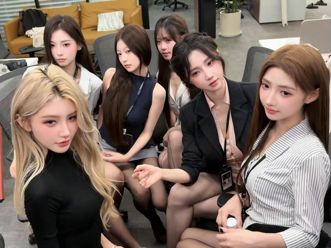 A group of six young women, mostly appearing to be of East Asian descent, posing together in what looks like an office or lounge setting.