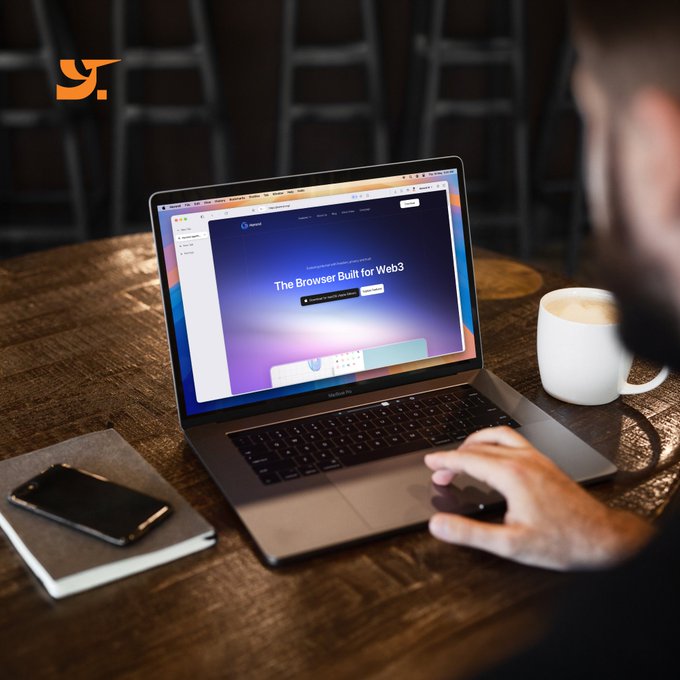 A person uses a MacBook Pro displaying the Opera website reading 'The Browser Built for Web3' with a 'Get it on Google Play' button, accompanied by a coffee mug and a phone on a wooden table.