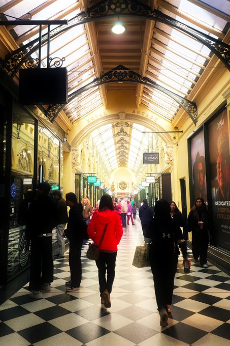 People walk through an ornate, historic shopping arcade with a black and white checkered floor, decorative ironwork, and glass ceiling, featuring signs for 'ARGYLE' and 'PANDORA'.