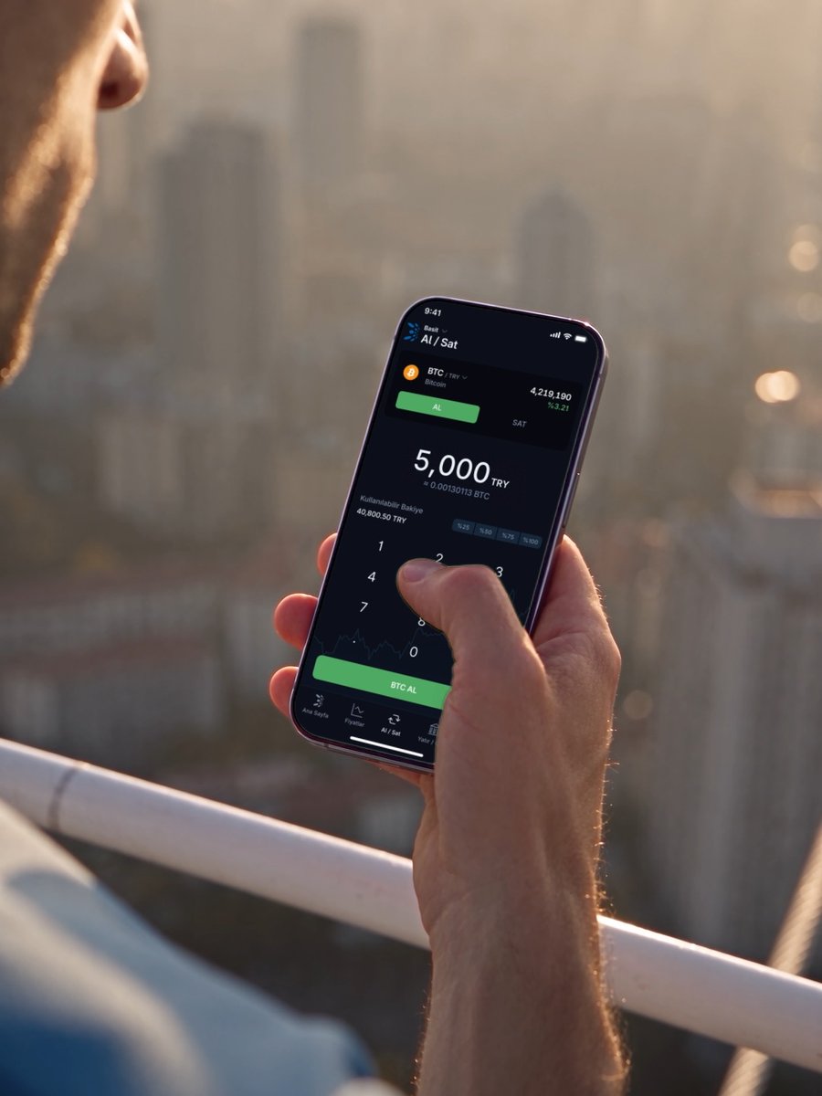 A man stands overlooking a hazy city skyline while using a cryptocurrency trading app on his smartphone, with the screen displaying a BTC/TRY buy interface at a price of 4,219,190 TRY and a 5,000 TRY trade amount. The image visually reinforces the post's message about how Basit's simple Al/Sat (Buy/Sell) feature lets users complete transactions with just a few taps by entering only an amount.