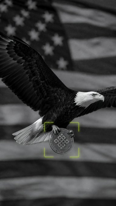 A black-and-white image shows a bald eagle in mid-flight clutching a coin or medallion, set against a softly blurred American flag backdrop. A green targeting bracket frames the coin, reinforcing themes of focus, recognition, and a milestone moment—mirroring the post's anticipation around Ritual's "Genesis 1,000" deployment of 2,000+ sovereign autonomous agents and the community rallying behind this pivotal achievement.