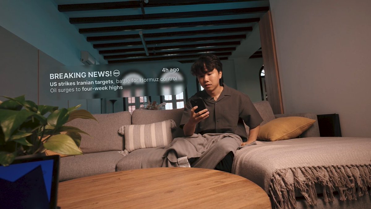 A young man sits on a couch looking at his phone, while a holographic breaking news alert floating beside him reads "BREAKING NEWS! 4h ago - US strikes Iranian targets, battle for Hormuz control, Oil surges to four-week highs." The image humorously contrasts the user's excitement about developments in "AgentFi" with a far more dramatic world event, suggesting that crypto/DeFi news may feel less thrilling compared to major geopolitical conflicts.