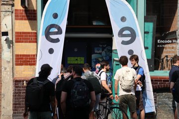 A group of people with backpacks gather outside a building between two banners displaying "e/9," with a "GREEN" sign visible in the window, at what appears to be an event space. The image ties to the post's wrap-up of Founder House London, showing attendees networking after a weekend of mentorship sessions and workshops supporting founders in the programmable economy.