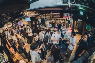 An overhead view of a crowded, dimly lit bar with numerous patrons gathered around the counter and socializing.