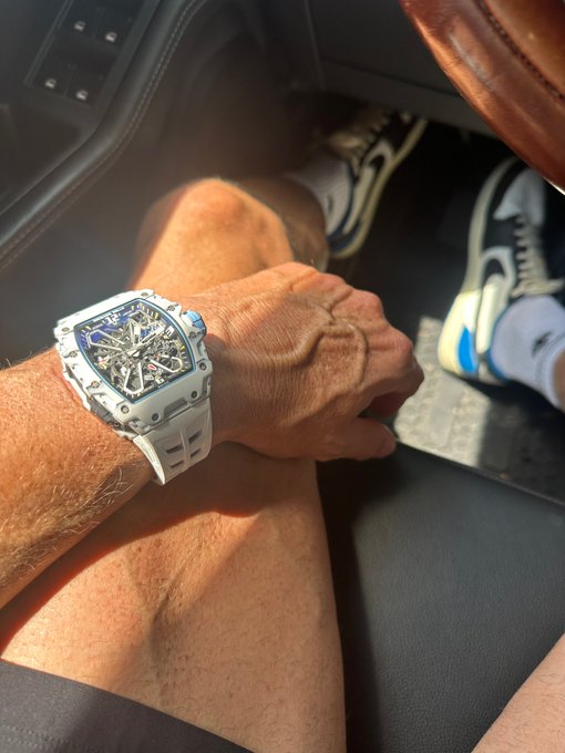 A person's wrist, resting on their bare leg inside a car, sports a luxury Richard Mille watch with a white rubber strap and skeleton face, paired with Nike Air Jordan sneakers visible in the background. The image visually reinforces the post's enthusiasm for high-end plastic watches and big wins.