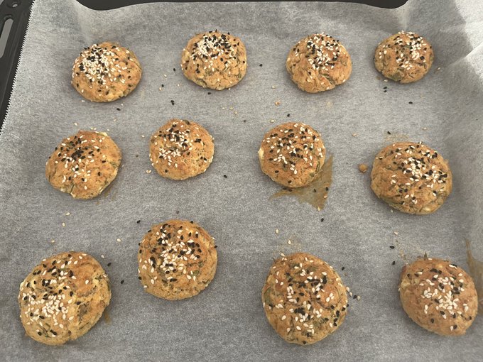 Twelve unbaked cookie dough balls topped with mixed sesame seeds are arranged on parchment paper, ready to go into the oven.
