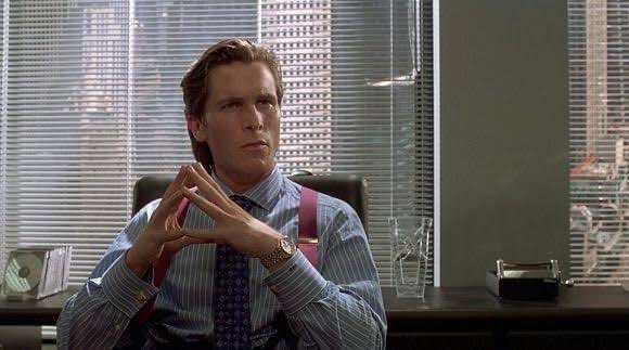 A still image from the movie American Psycho showing Patrick Bateman (Christian Bale) sitting in his office, wearing a striped shirt, suspenders, and a patterned tie, with his fingers steepled together.