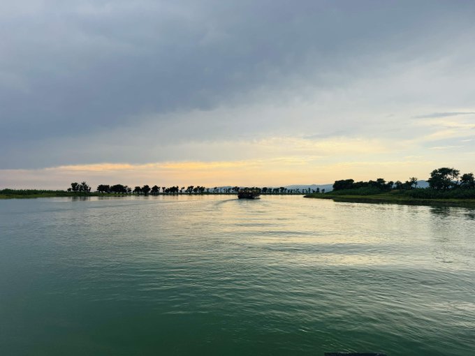 The image shows a beautiful view of a river with trees lining its banks. The sky above the water has an orange hue, suggesting that the photo was taken during sunset or sunrise. In the background, there are several boats floating on the water, adding to the picturesque scene. The caption provided in the image seems unrelated and does not provide any context about the content of the photo.