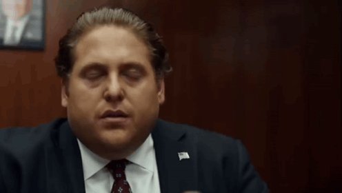 The image shows a man wearing a suit, sitting at a desk with his eyes closed while looking down at something off-camera. The background features a wooden wall, suggesting that they are in an office or a professional setting. There is also text on the image that reads "i was fixing the automations in @axiegoodness and on another tab buying x premium+ for my personal account ended up buying premium+ for @axiegoodness instead". This implies that the man might be involved in some form of online business or discussion related to the "@axiegoodness" account.