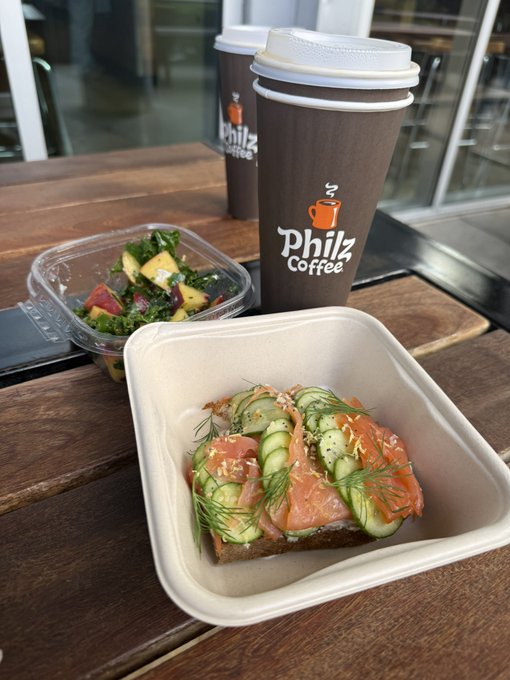 A Philz Coffee meal setup features two branded cups, a side salad, and an open-faced sandwich topped with smoked salmon and cucumbers on a wooden table.