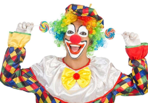 A cheerful clown with a rainbow wig holding two swirled lollipops, wearing a colorful diamond-patterned costume with a large yellow bow.