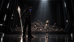 Two figures stand facing each other in a dimly lit futuristic corridor, with the taller figure on the left holding a glowing spear and glowing blue eyes, casting light onto the reflective floor.
