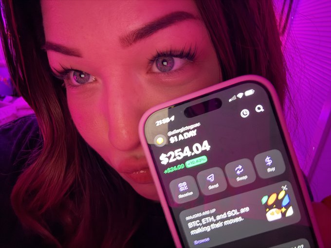 A close-up photo shows a person with purple-lit hair and makeup holding a smartphone that displays the $1ADY token at a price of $254.04, up +524.00%, with a section about MAJOR, ETH, and SOL making moves.