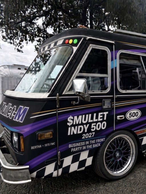 A photograph of a black and purple customized van with racing stripes and checkerboard patterns, bearing the text '$MULLET INDY 500 2027', 'BUSINESS IN THE FRONT PARTY IN THE BACK', and 'BERTHA - 1975 FMC'.