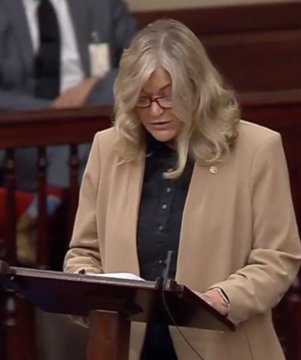 Senator Cynthia Lummis, wearing a tan blazer and glasses, stands at a podium reading from documents during a formal address regarding the CLARITY Act, a piece of legislation she champions to establish U.S. regulatory leadership over digital assets.