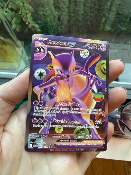 A hand holding a holographic Mewtwo EX Pokémon trading card with 230 HP, featuring moves 'Photon Bullets' and 'Psychic Powers.'