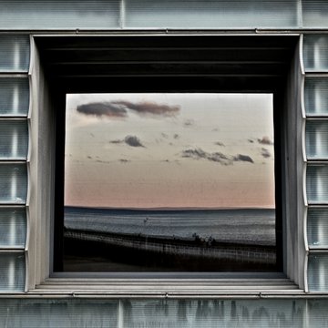A view of a serene sunset over the ocean, framed by a square industrial window. The image evokes the "horizon" and "interdiction" themes referenced in the post promoting two NFTs listed on OpenSea at 0.15 ETH.