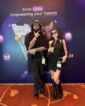 Two people posing in front of an 'Envo Live' backdrop that reads 'Empowering your Talents' with phone imagery and the year '23'.