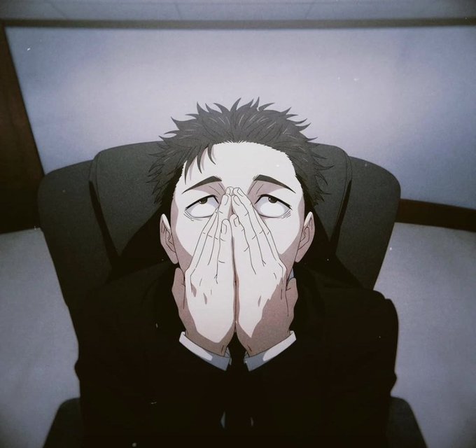 An anime character with dark spiky hair sits in a chair, hands clasped together covering the lower half of his face, with an intense, wide-eyed expression.