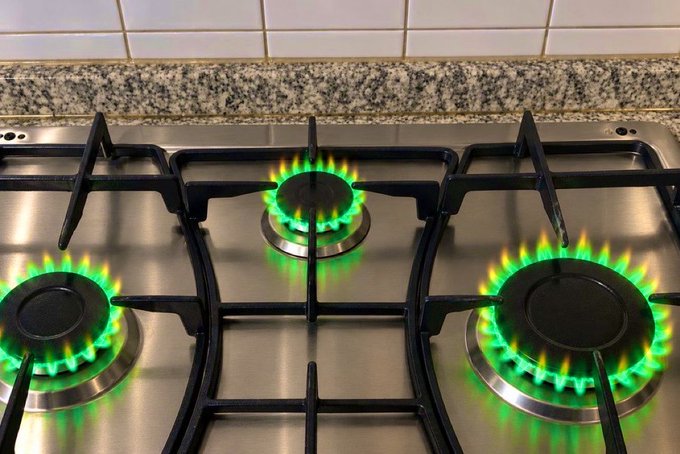 A stainless steel gas stove has three burners lit with bright green flames.