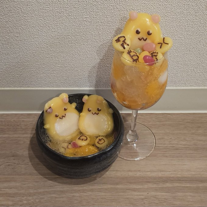 Two adorable yellow chick-shaped desserts or jellies served in a small bowl alongside a tall glass containing an orange drink and another chick-shaped jelly on top.