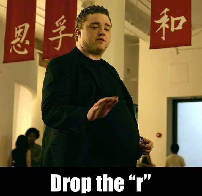 The image shows a man in a black suit standing in front of red banners with Chinese characters, with the caption "Drop the 'r'" displayed at the bottom. The meme humorously parodies Kanye West's famous Taylor Swift VMAs interruption, with "Drop the 'r'" suggesting a rebrand from "Fartcoin" to "Fatcoin," aligning with the post's playful claim that Fatcoin will surpass Fartcoin as one of the best memecoins.