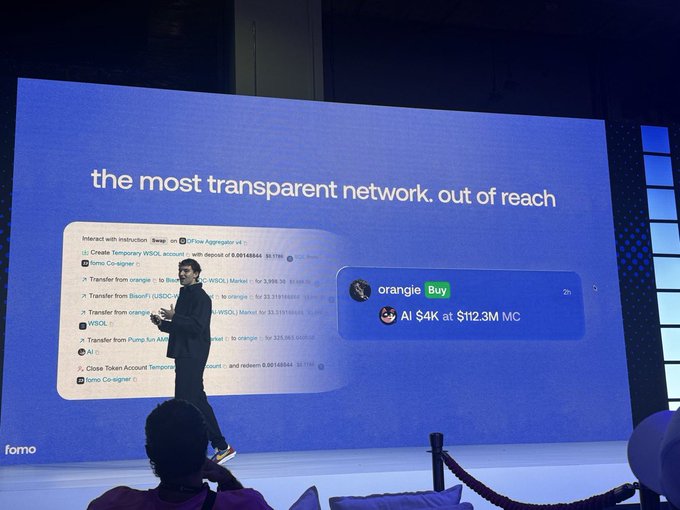 A presenter stands on stage in front of a large screen displaying "the most transparent network. out of reach," which highlights a swap of $4k worth of $AI at a $112.3M market cap, aligning with the post's mention of $AI gaining attention at an early stage.