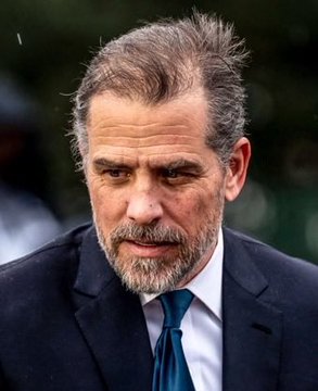 A close-up portrait of an older man with graying hair and beard, wearing a dark suit and teal tie, looking downward with a serious expression.