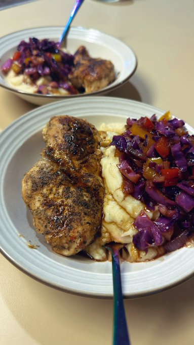 Two bowls contain seasoned blackened chicken breasts served over mashed potatoes with purple cabbage and bell pepper slaw.