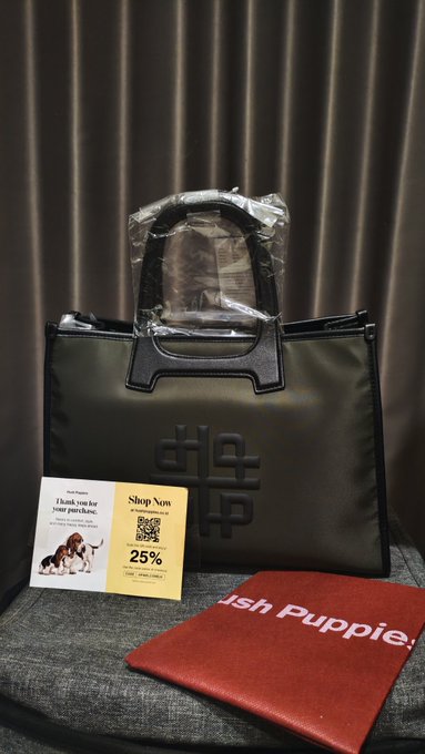 A black tote bag with a quilted logo design is displayed alongside a Shopee promotional card offering "25%" off and a red pouch labeled "ish Puppie." The post describes it as a thoughtful gift from a friend, noting it's finally a proper women's bag beyond work or crypto merch totes.