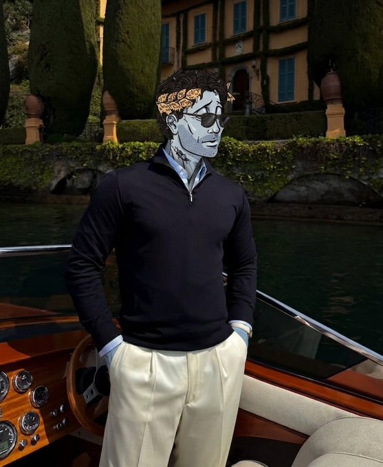 A man wearing a black quarter-zip sweater and white trousers stands on a wooden boat, with a digitally added illustrated face wearing sunglasses and a laurel wreath, against a backdrop of a villa and water.