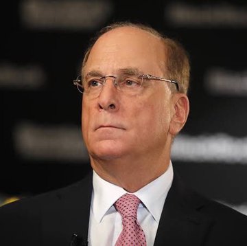 A close-up portrait of a man with glasses, wearing a suit and pink tie, appearing to be at a formal event.